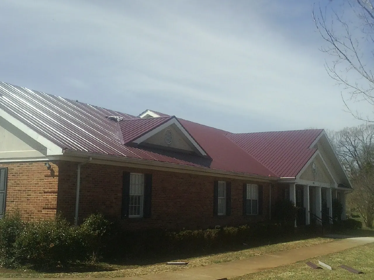 Red metal roof with gabled entries on a long brick building, from a Hail Damage Roof Repair job in Manzanita