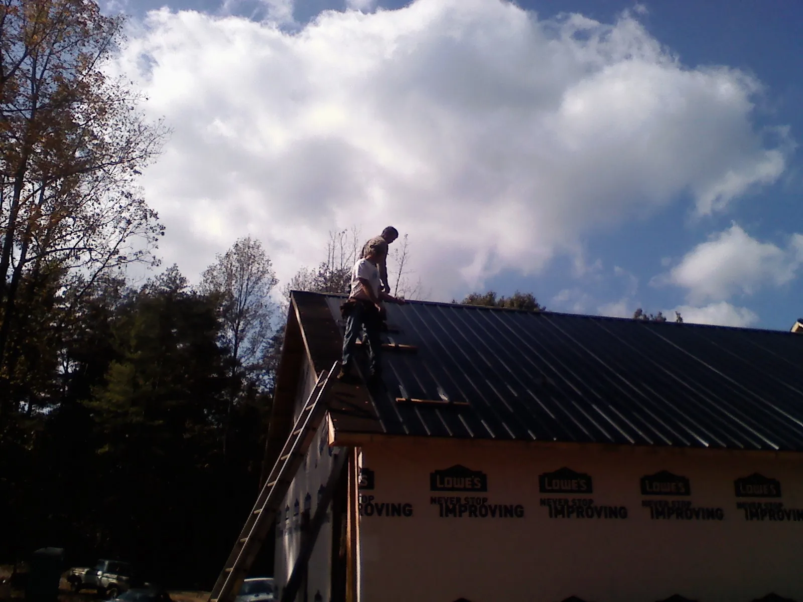 Roofer fastening dark metal panels high against a cloudy sky, from a Roof Inspection job in Manzanita