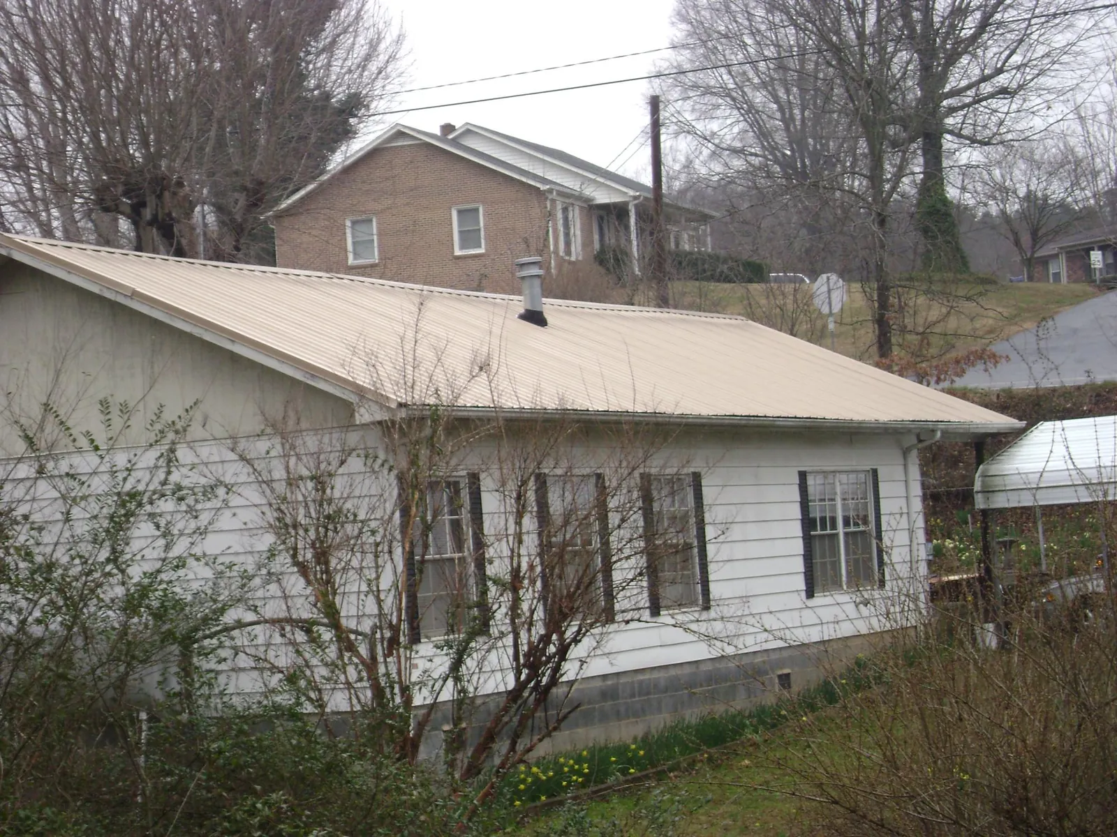 Tan metal roof on a white sided house set into a hillside — Commercial Roofing by Roofing Brothers in Manzanita